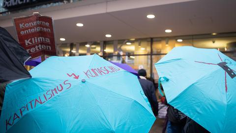 Ein Demonstrant steht mit einem Schirm, auf welchem "Kapitalismus, Klimaschutz" steht vor der Baden-Württembergischen Bank während der Demonstration am Globalen Klima Aktionstag.