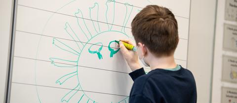 Ein Schüler zeichnet ein Coronavirus an die Tafel.