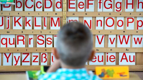 Ein Kind sitzt an einem Tisch, auf dem im Hintergrund Buchstaben zu sehen sind.