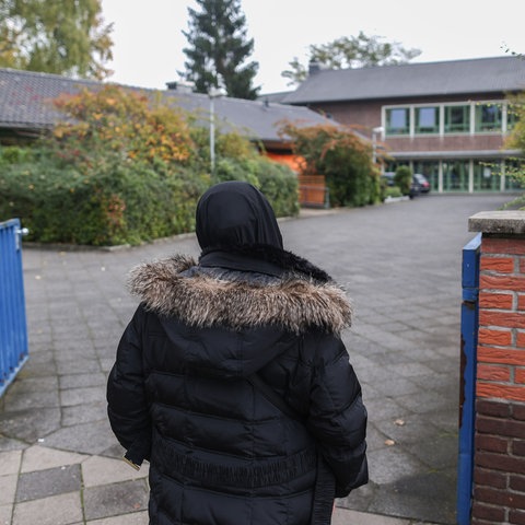 Eine Frau mit Kopftuch steht vor einer Schule