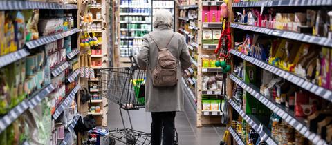 Eine Frau geht mit ihrem Einkaufswagen durch einen Supermarkt.