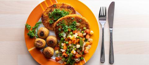 Falafel, vegane Schnitzel und Gemüse liegen garniert mit Petersilie auf einem Teller