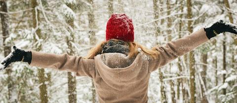 Frau breitet Arme aus vor Winterwald