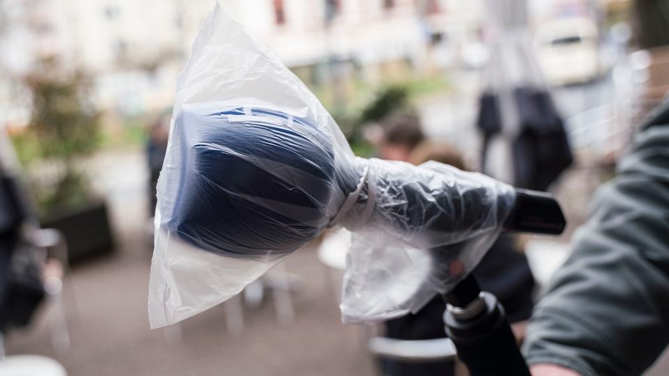 Ein Fernsehjournalist des Hessischen Rundfunks hält bei einer Reportage über die Auswirkungen im öffentlichen Leben in Zeiten der Verbreitung des Coronavirus ein Mikrofon, das mit einer Plastiktüte vor Viren geschützt werden soll.